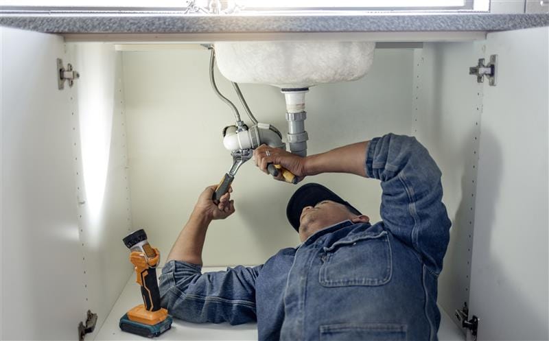 Plumber repairing pipes beneath a bathroom sink in Paramount